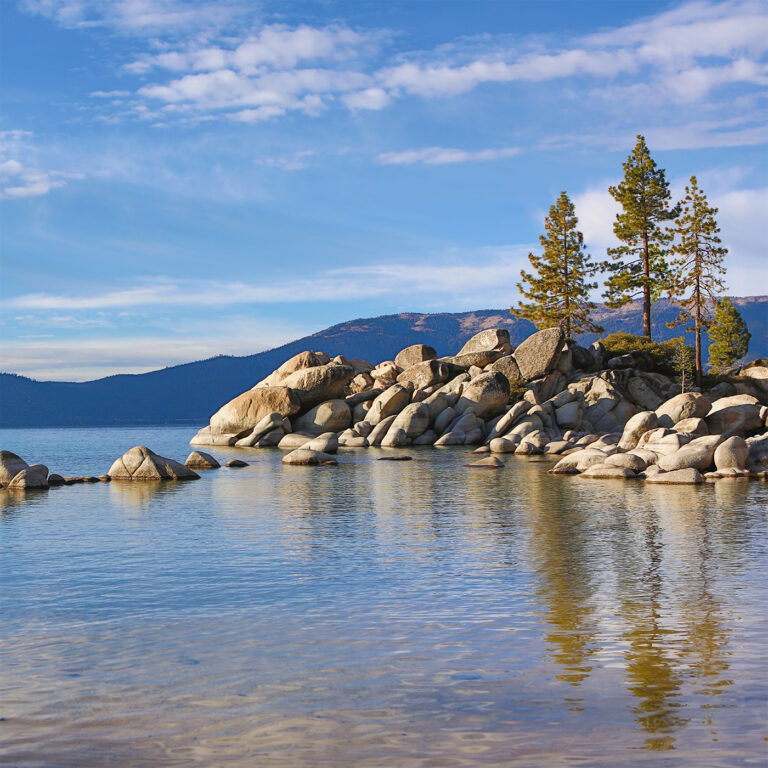 Full bleed digital photography preview of a pristine summer evening at Sand Harbor on Lake Tahoe, showcasing clear water, smooth boulders, and distant Sierra Nevada mountains.