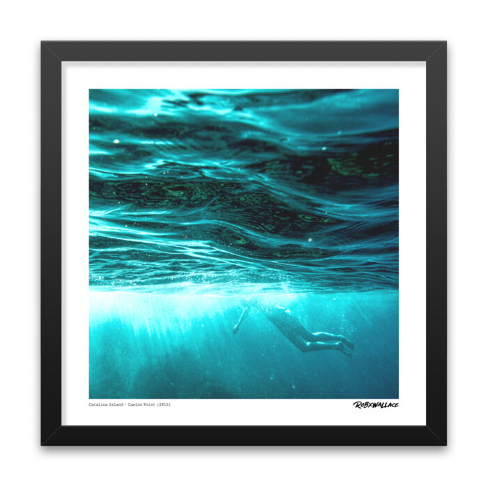 Close up view of an 18x18 square framed marine art print showing sunlight filtering through clear blue water with a distant swimmer on the California coast.