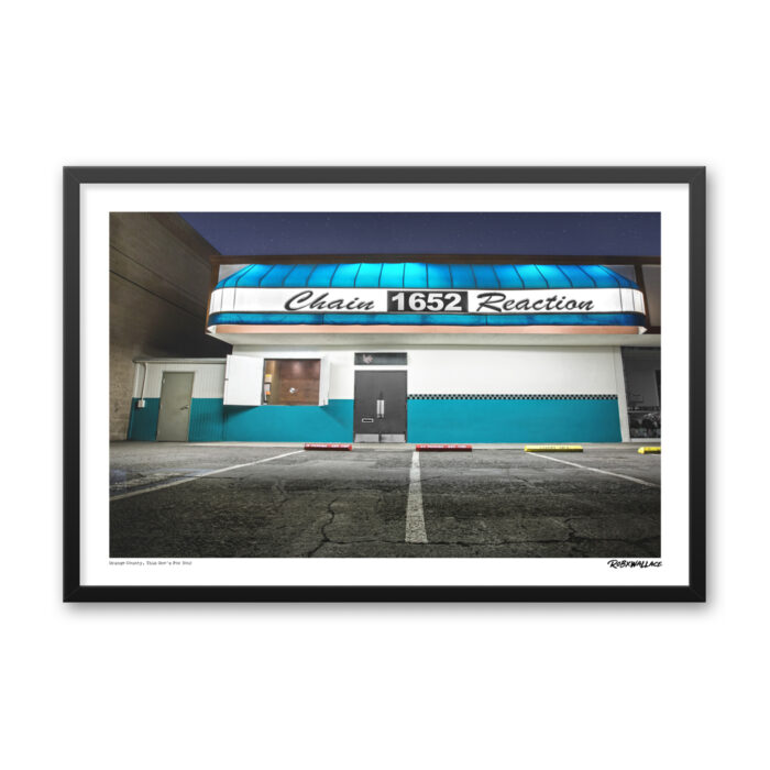 Close up view of a 24x36 wide framed music venue poster print showcasing the storefront of Chain Reaction lit up at night.
