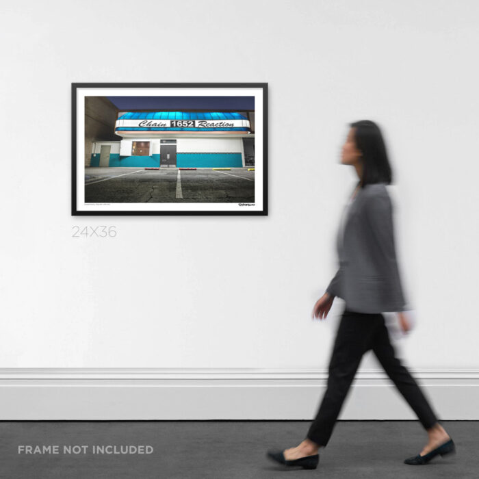 24x36 wide framed Graphic Design print the exterior facade of Chain Reaction in Anaheim at night, displayed on an art gallery wall for scale.