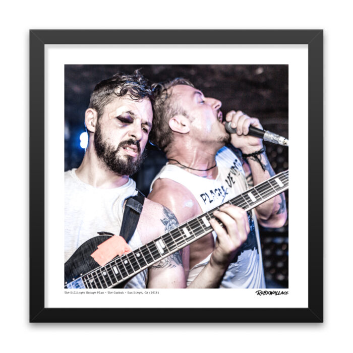 Close up of an 18x18 square framed metal documentary wall art print showcasing guitarist Ben Weinman pushing through an intense live set with a black eye alongside Greg Puciato.