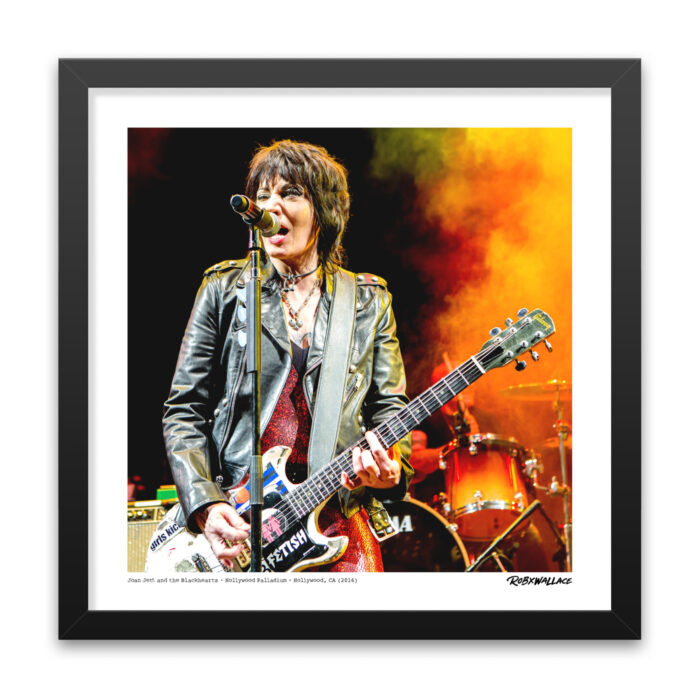 Detailed close-up view of an 18x18 square framed rock history print showcasing Joan Jett performing in her signature leather jacket and shimmering red outfit against fiery red and yellow stage lights.