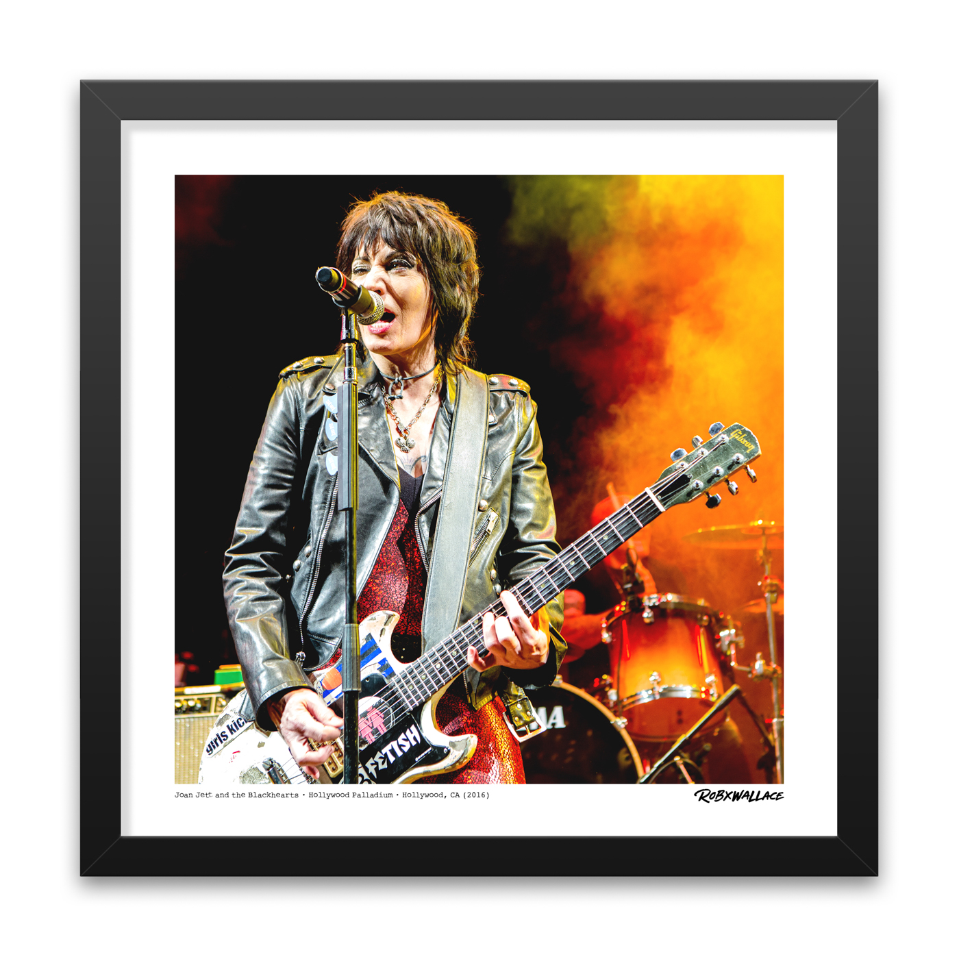 Detailed close-up view of an 18x18 square framed rock history print showcasing Joan Jett performing in her signature leather jacket and shimmering red outfit against fiery red and yellow stage lights.